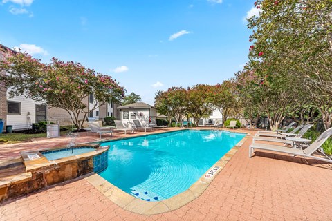 A swimming pool surrounded by a brick patio and lounge chairs.