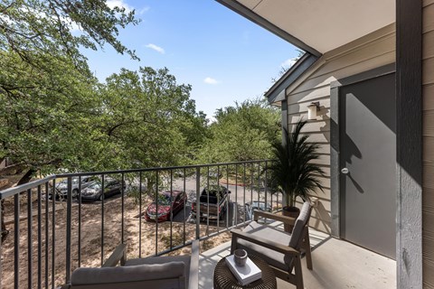 A patio with a chair and table overlooking a parking lot.