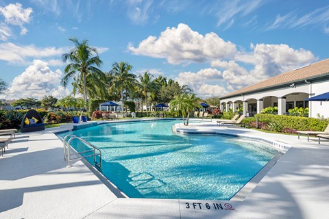 A large outdoor swimming pool with lounge chairs and an adjacent clubhouse overlooking a body of water