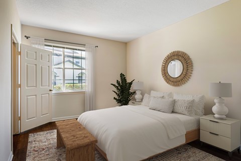 A bedroom with a white bed, a wooden bench, and a round mirror on the wall.