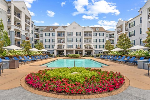 A large pool surrounded by a flower bed in front of apartment buildings.