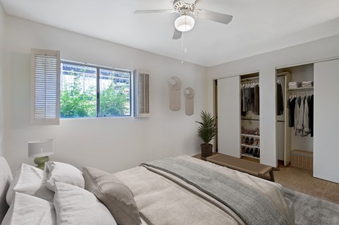 A bedroom with a large bed and a closet with clothes.