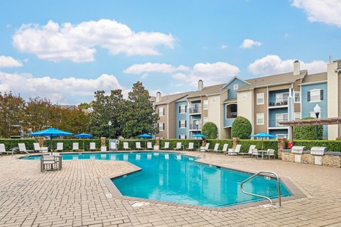 A swimming pool surrounded by lounge chairs and umbrellas in front of apartment buildings.