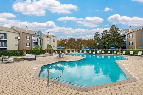 A large swimming pool surrounded by a brick patio and lounge chairs.
