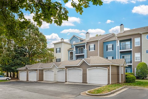 A row of apartments with detached garages in front of a tree.