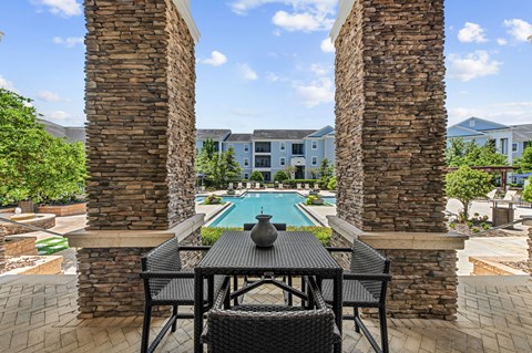 A table with chairs is in the foreground of a pool area.