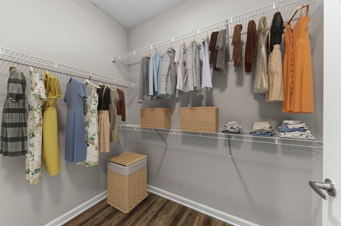 A white closet with clothes hanging and a basket on the floor.