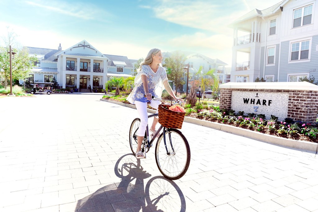 A woman riding a bike in front of a sign that says at Wharf 7 Apartments, Charleston
