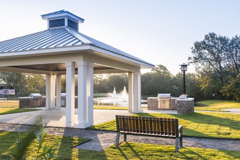 A gazebo with a fountain in the background and a bench in the foreground.