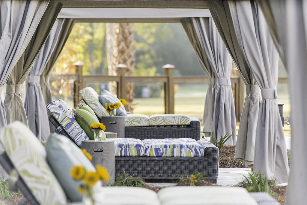 A patio with grey curtains and a couch with a yellow flower on it at Wharf 7 Apartments, Charleston, SC