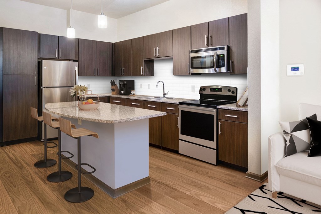 a kitchen with dark wood cabinets and a white island with a granite countertop a kitchen with dark wood cabinets and a white island with a granite countertop at The Rialto, Orlando, FL, 32819