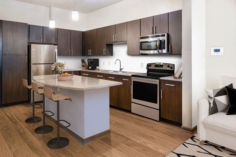 a kitchen with dark wood cabinets and a white island with a granite countertop at The Rialto, Orlando, FL, 32819