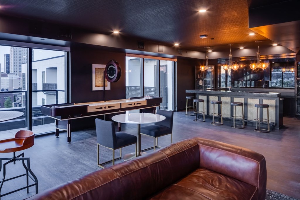 a living room with a brown leather couch and a bar with tables at Maven on Broadway, Rochester, 55904