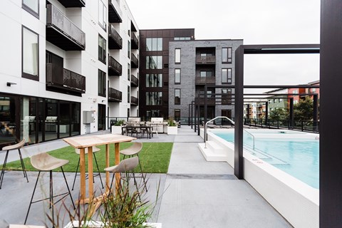 A modern outdoor seating area with a pool and apartment buildings in the background.