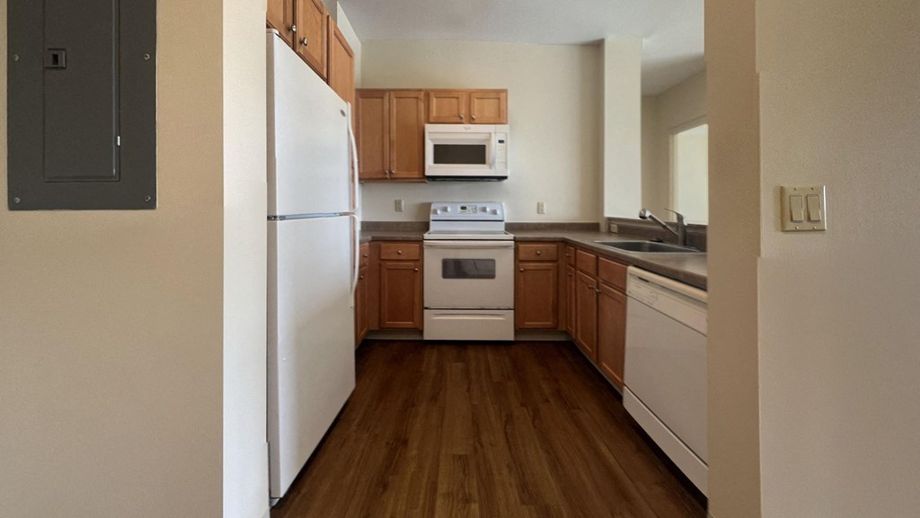 an empty kitchen with wooden floors and white appliances