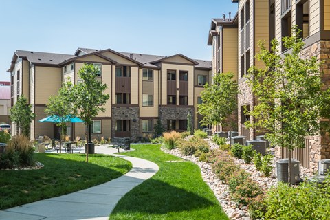 a sidewalk leading to an apartment building with lush green grass and trees at Estate at Woodmen Ridge, Colorado Springs, CO 80923