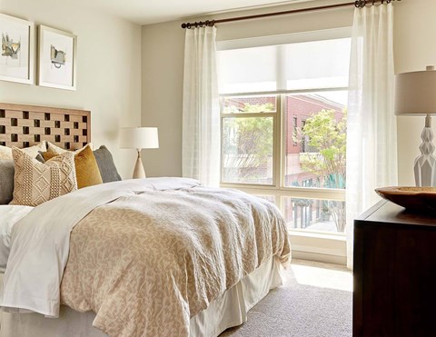 A bedroom with a large bed and a view of a red building outside the window.