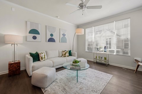 A living room with a white couch, a glass coffee table, and a ceiling fan.