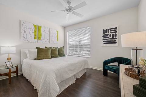 A bedroom with a bed, chair, and artwork on the wall.