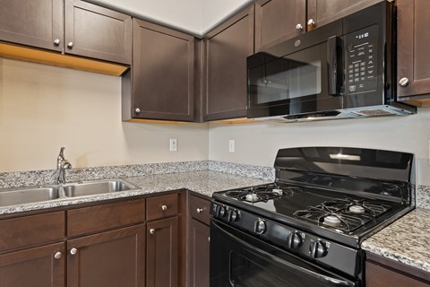 A black microwave is mounted above a black stove in a kitchen.