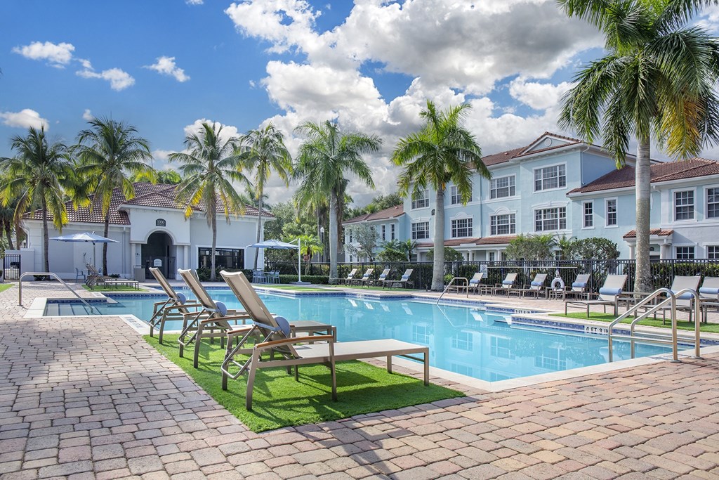 A pool surrounded by palm trees and lounge chairs.
