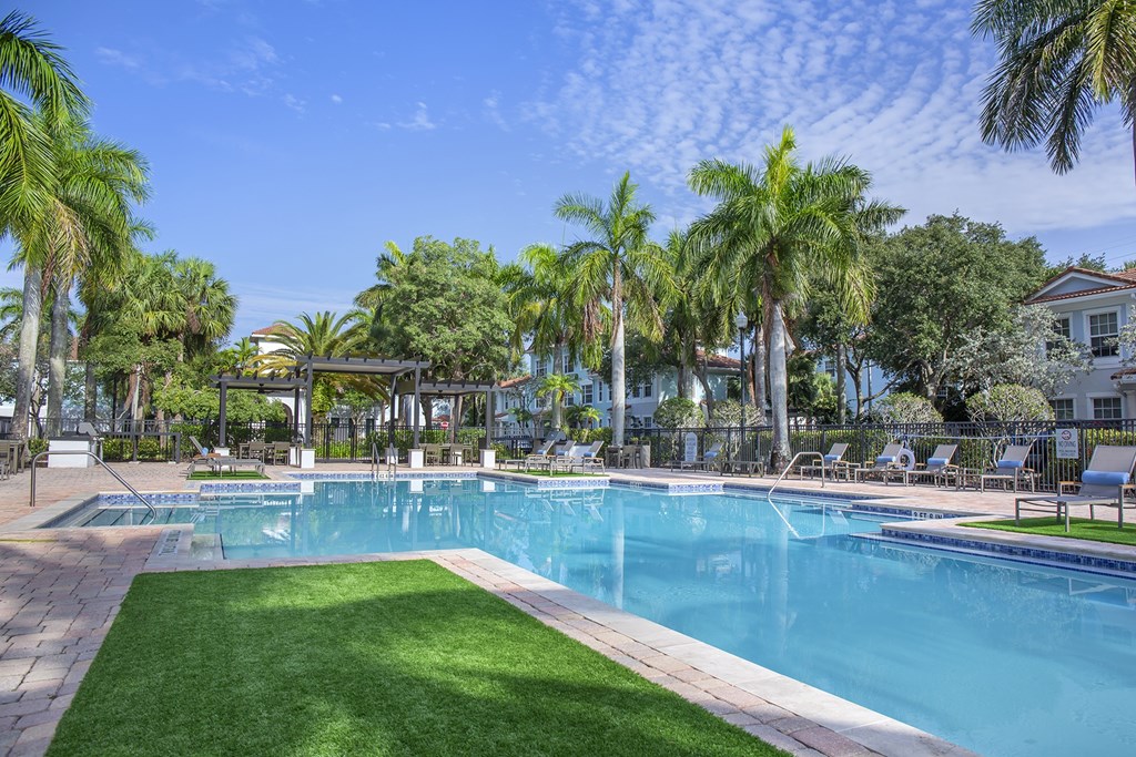 A large swimming pool surrounded by palm trees and lounge chairs at Floresta apartments in Jupiter, FL