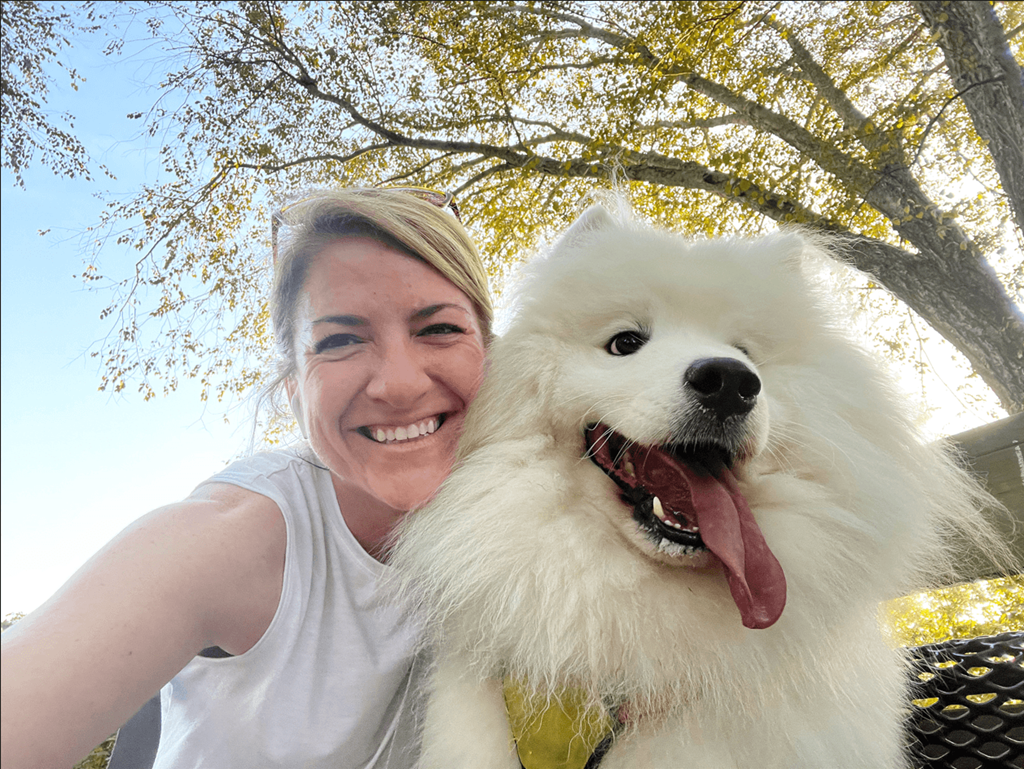 a woman holding a white dog with its tongue out