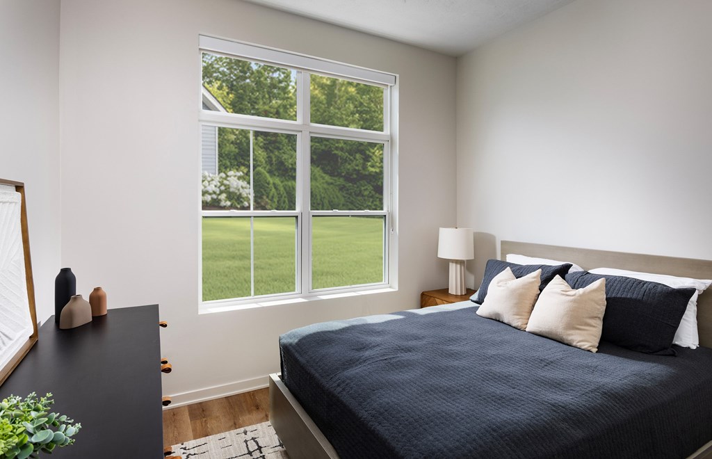 A bedroom with a large window overlooking a green lawn.
