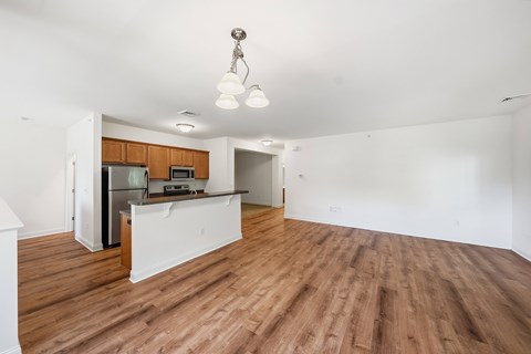 A room with wooden floors and a kitchen area with a refrigerator, microwave, and oven.