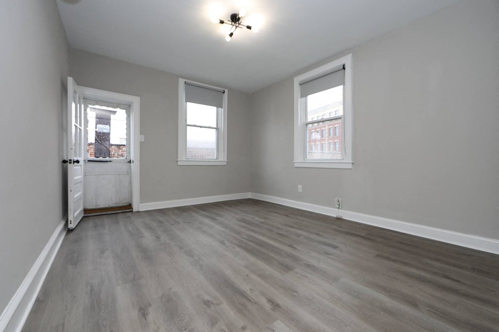an empty living room with a door and two windows