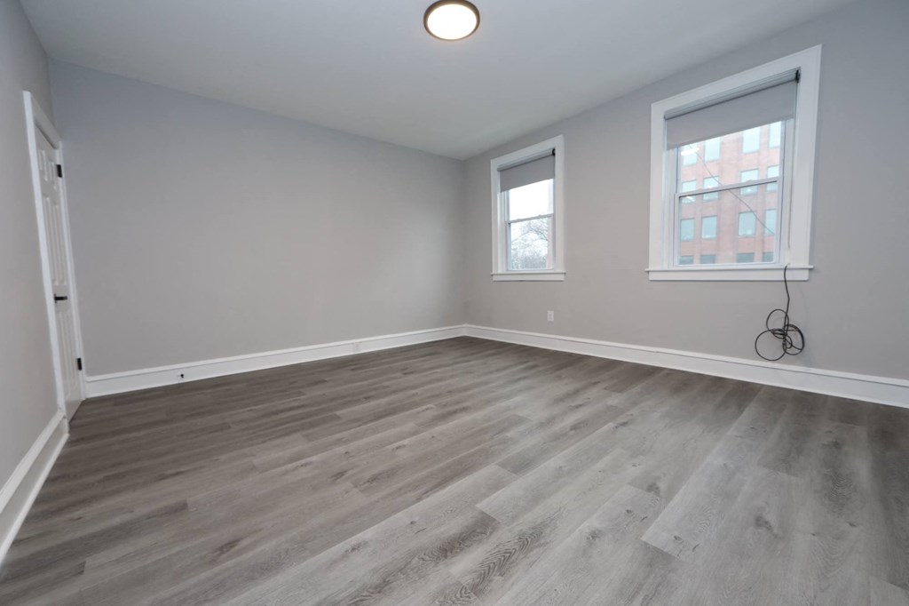 an empty living room with wood flooring and two windows