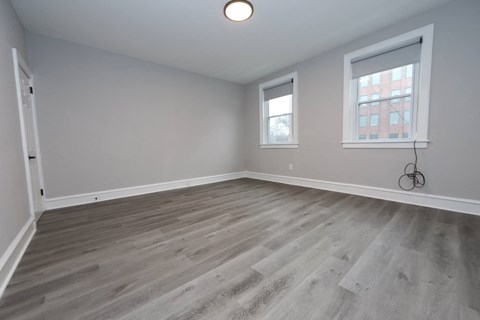 an empty living room with wood flooring and two windows