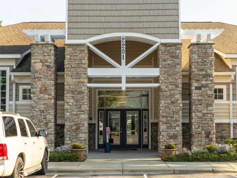 A white car is parked in front of a building with a stone pillar and a white arched entrance.