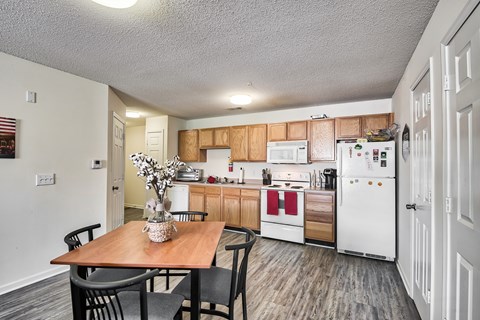 A kitchen with a table and chairs in the foreground and a refrigerator, microwave, and oven in the background.