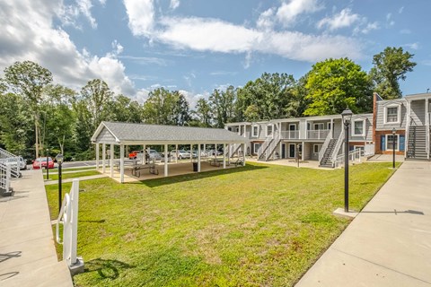 A sunny day at a park with a building and a picnic table.