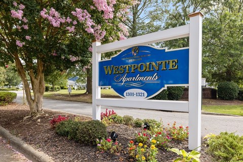 A sign for Westpointe Apartments is displayed in front of a tree with pink flowers.
