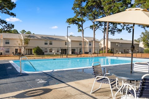 A pool area with chairs and an umbrella in front of apartment buildings.