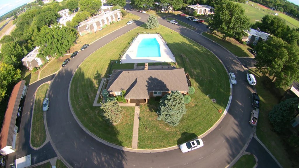 A bird's eye view of a residential area with a house, swimming pool, and cars.