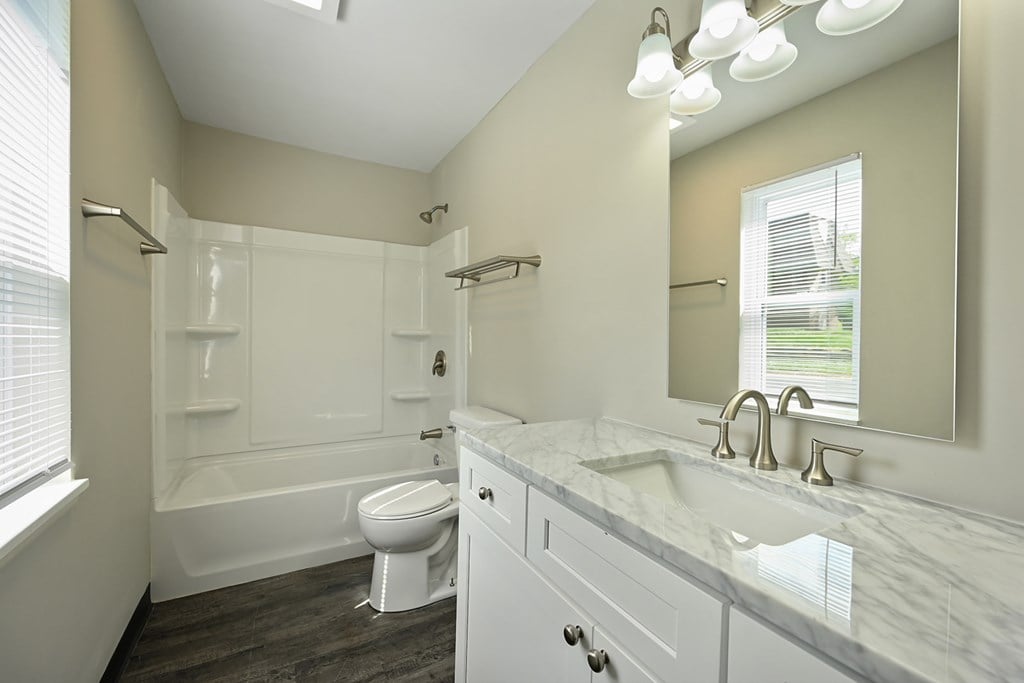 A white bathroom with a marble counter top and a toilet.