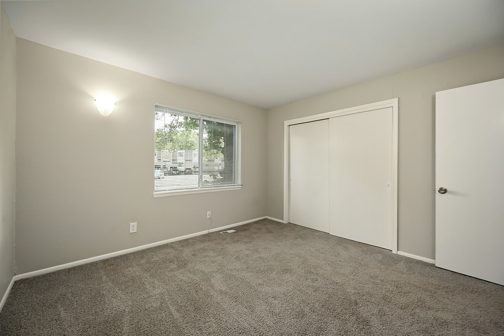 A room with a carpeted floor and a window with blinds.