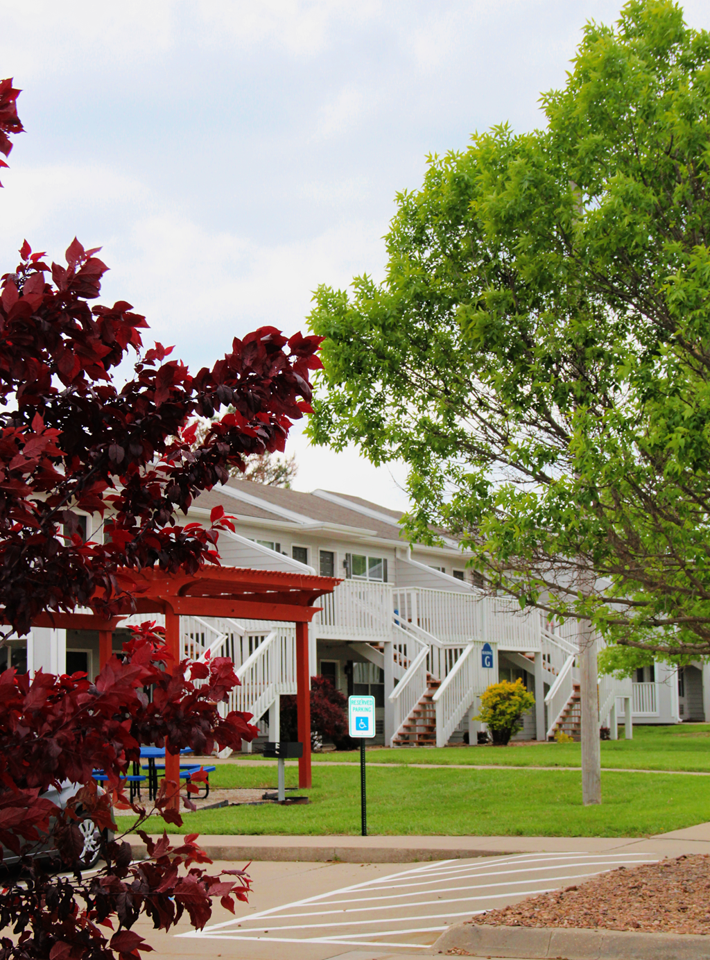 A tree with red leaves is in front of a white building with a covered staircase.