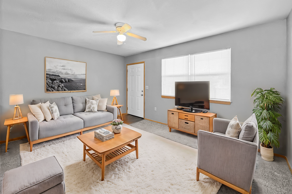 A living room with a grey couch, a wooden coffee table, a grey armchair, a wooden cabinet, a television, a plant, and a painting on the wall.