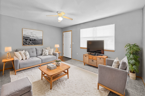 A living room with a grey couch, a wooden coffee table, a grey armchair, a wooden cabinet, a television, a plant, and a painting on the wall.