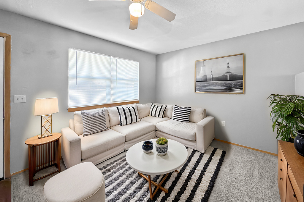 A living room with a white couch, a small table, and a ceiling fan.