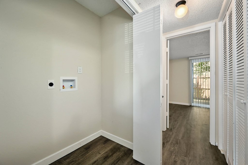 an empty room with white walls and wood flooring and a door to a hallway