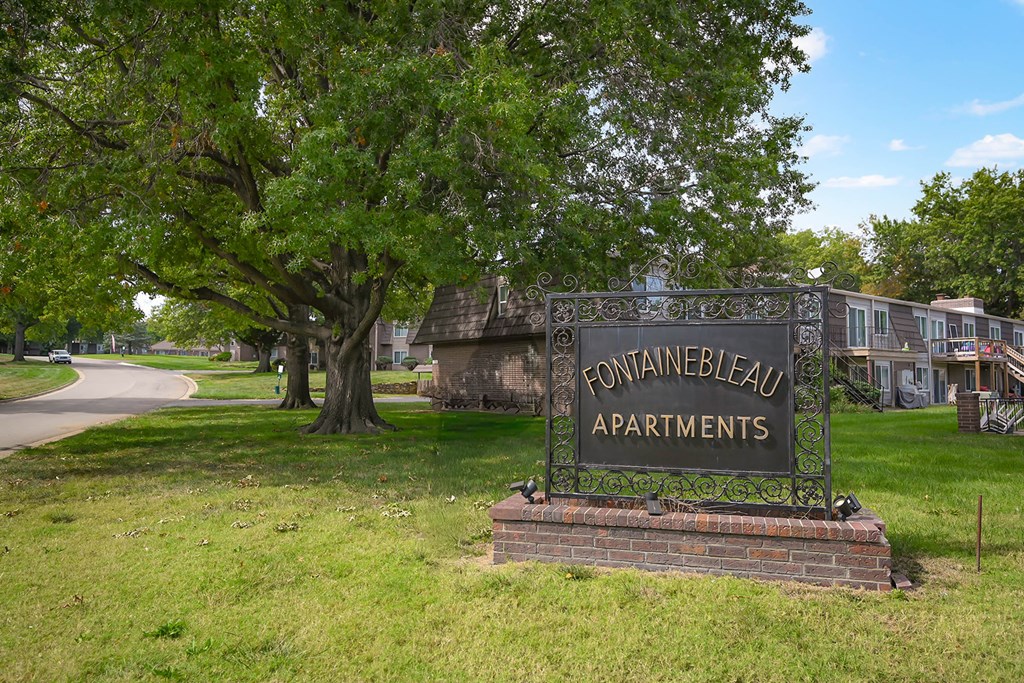 A sign that says "Fontainebleau Apartments" in front of a grassy area.