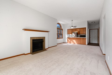 an empty living room with a fireplace and a kitchen