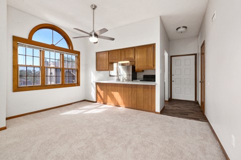 an empty living room with a kitchen and a ceiling fan