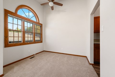 an empty living room with a large window and a ceiling fan