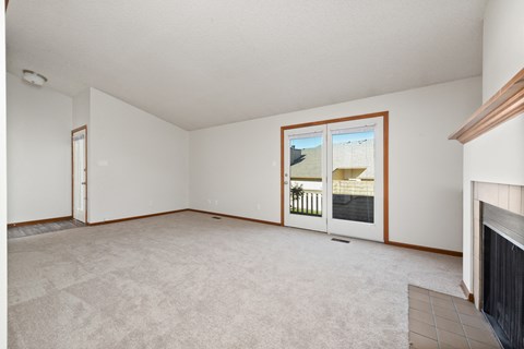 an empty living room with a fireplace and a door to a balcony